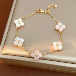 Dettaglio di un bracciale dorato con ciondoli a fiore rosa ciliegio e pietre di zircone