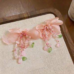 Close-up of elegant pink floral fabric earrings with beaded tassel and green leaf accents