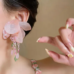 Detail shot of a pink fabric flower earring with beaded tassels worn by a model