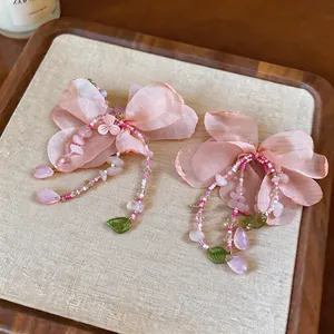 Close-up detail showing pink fabric flower earrings with delicate beads and green leaf charms