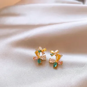 Macro view of colorful butterfly zircon stud earrings displayed on soft silk fabric.