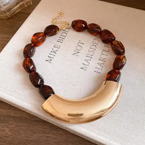 Detail shot of a vintage acrylic beaded necklace featuring a curved gold metal pendant (84 chars)