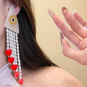 Detailed view of vintage resin pearl tassel earrings with red heart charms and gold accents.