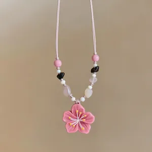 Detailed view of the pink cherry blossom pendant and decorative geometric beads.