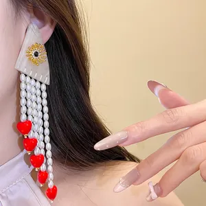 Detailed view of long pearl tassel earrings with red hearts and golden sun motif
