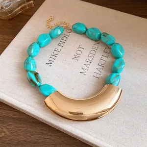 Macro detail of turquoise acrylic beads and curved gold pendant on a vintage book