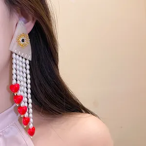 Close-up of elegant long pearl tassel earrings with red heart charms on a model