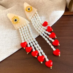 Detail of pearl tassel earrings with vibrant red heart charms and gold sun motif.