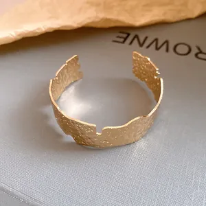 Close-up detail of a minimalist textured gold open cuff bracelet with an irregular design
