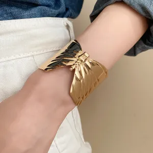 Detailed view of a gold-toned butterfly cuff bracelet with a pleated wing design worn on wrist