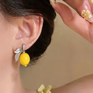 Detailed view of a bright yellow lemon earring with micro-set zircon leaves on an ear