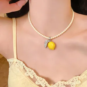 Detailed view of an elegant pearl necklace featuring a vibrant yellow lemon pendant on a model