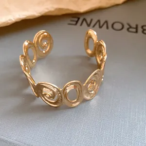 Detail shot of a gold open cuff bracelet with irregular swirl and oval patterns.