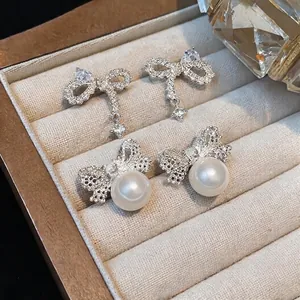 Elegant silver-tone zircon bow and pearl stud earrings displayed in a jewelry box.