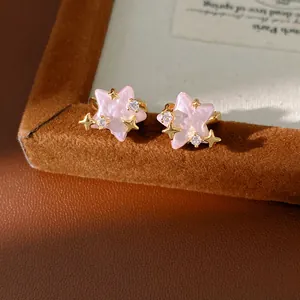 Dettaglio di orecchini a stella rosa perlati con accenti di zirconi e stelle d'oro