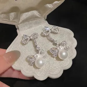 Elegant silver needle bow earrings with shimmering zircons and round white pearls in a shell box