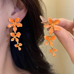 Detailansicht der leuchtend orangefarbenen Emaille-Blumenohrringe am Ohr eines Models
