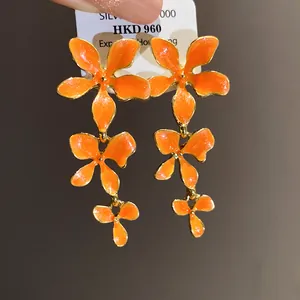 Detaillierte Makroansicht von leuchtend orangefarbenen Emaille-Blumen-Quastenohrringen.
