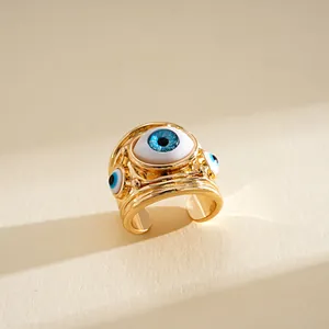 Dettaglio di un anello dorato aperto con motivo a occhio in resina blu e metallo