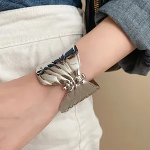 Close-up of a stylish shiny silver wrinkled butterfly cuff bracelet worn on the wrist.