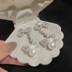 Macro view of elegant silver zircon bow pearl earrings resting in a white shell box