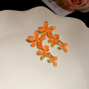 Detailansicht von orangefarbenen Emaille-Blumen-Ohrringen mit Goldrand auf einem weißen Teller