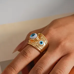Dettaglio ravvicinato di un anello dorato con due occhi in resina indossato sul dito.