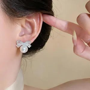 Exquisite close-up detail of silver zircon bow earrings with elegant white pearl drops