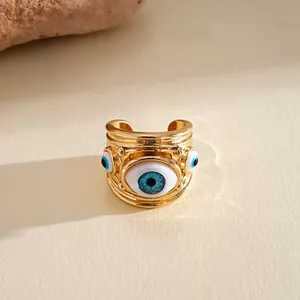 Vista ravvicinata di un anello aperto dorato decorato con motivi di occhi in resina blu