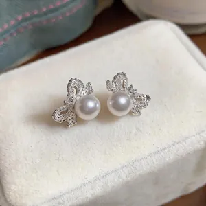 Detailed macro shot of elegant bow-shaped pearl stud earrings on white velvet