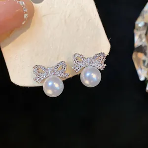 Elegant close-up detail of bow-knot pearl stud earrings with sparkling zircon inlay