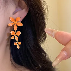 Detailansicht der orangefarbenen Emaille-Blumen-Quastenohrringe mit edlem Goldrand am Model.