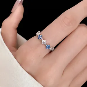 Detailed view of silver zircon open ring with blue clover motifs worn on finger.