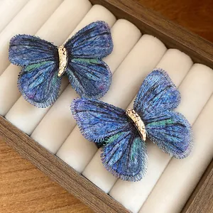 Close-up of two blue embroidered butterfly hair clips in a wooden jewelry tray display