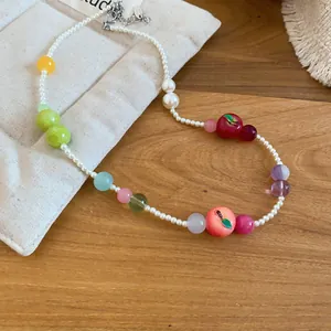 Detailed close-up of French resin apple and peach beaded pearl necklace on a wood surface