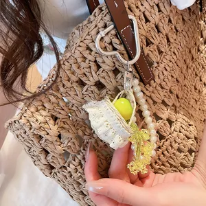 Detail view of resin green apple keychain with pearls and lace basket on straw bag