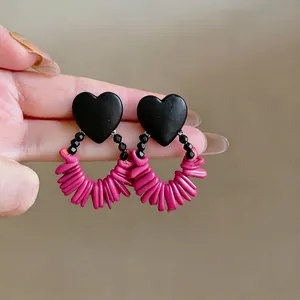 Retro heart-shaped wooden earrings with vibrant pink fringe detail held by hand.