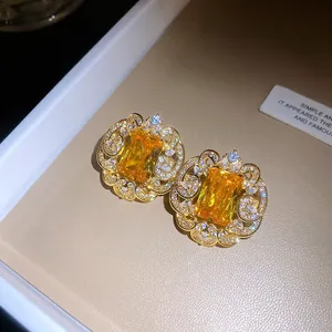 Gros plan de boucles d'oreilles en dentelle dorée avec une gemme rectangulaire jaune