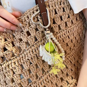 Close-up detail of a sweet French resin apple and pearl charm pendant on a woven straw bag.