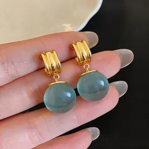 Close-up van retro goudkleurige oorbellen met doorschijnende blauwgroene harsbollen.