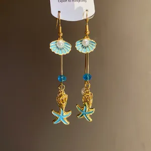 Detail view of gold-plated beach style earrings featuring blue shell and starfish pendants