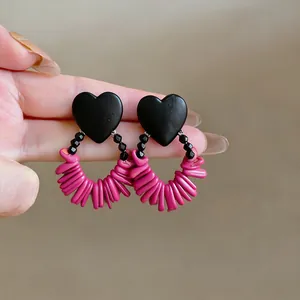 Detail view of retro black wooden heart earrings with pink magenta fringed hoops