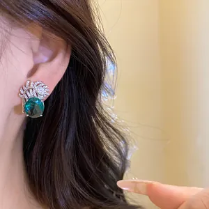 Dettaglio in primo piano di orecchini vintage a piuma con zircone verde sull'orecchio