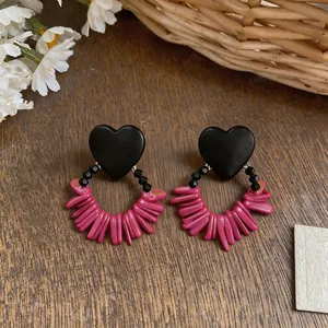 Close-up detail view of retro black heart earrings with vibrant pink bead fringe