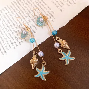 Macro view of blue enamel starfish and shell charms on golden dangle earrings