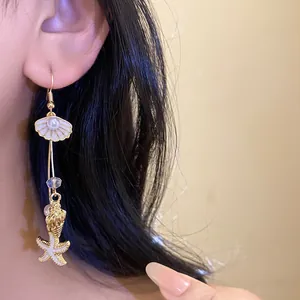 Detail view of golden seashell and starfish drop earrings with pearls worn by model