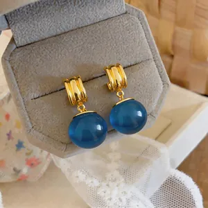 Detailopname van vintage gouden oorbellen met grote doorschijnende blauwe harsballen
