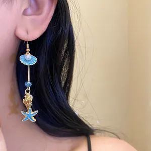 Close-up detail of a blue enamel shell and starfish drop earring worn by a model