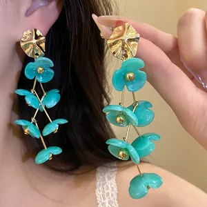 Close-up of turquoise acrylic flower dangle earrings with gold-tone metal studs.