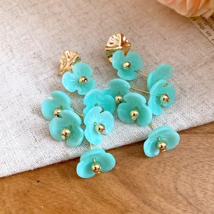 Close-up detail of light blue acrylic flower drop earrings featuring elegant golden beads